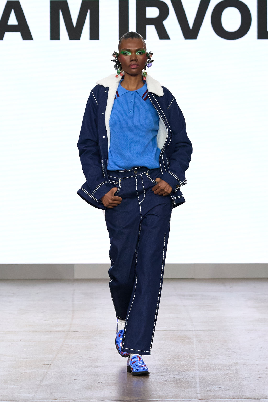 Model wearing dark blue high-waisted trousers with light contrast stitching on the catwalk.