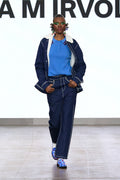 Model wearing dark blue high-waisted trousers with light contrast stitching on the catwalk.