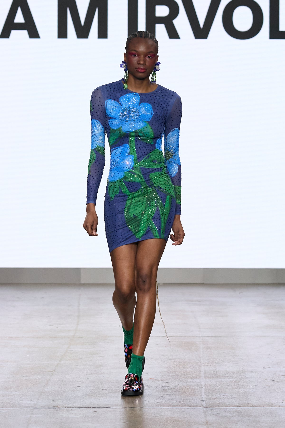 Model wearing the long-sleeved Blue Bloom Dress with blue flowers and green leaves on the catwalk.