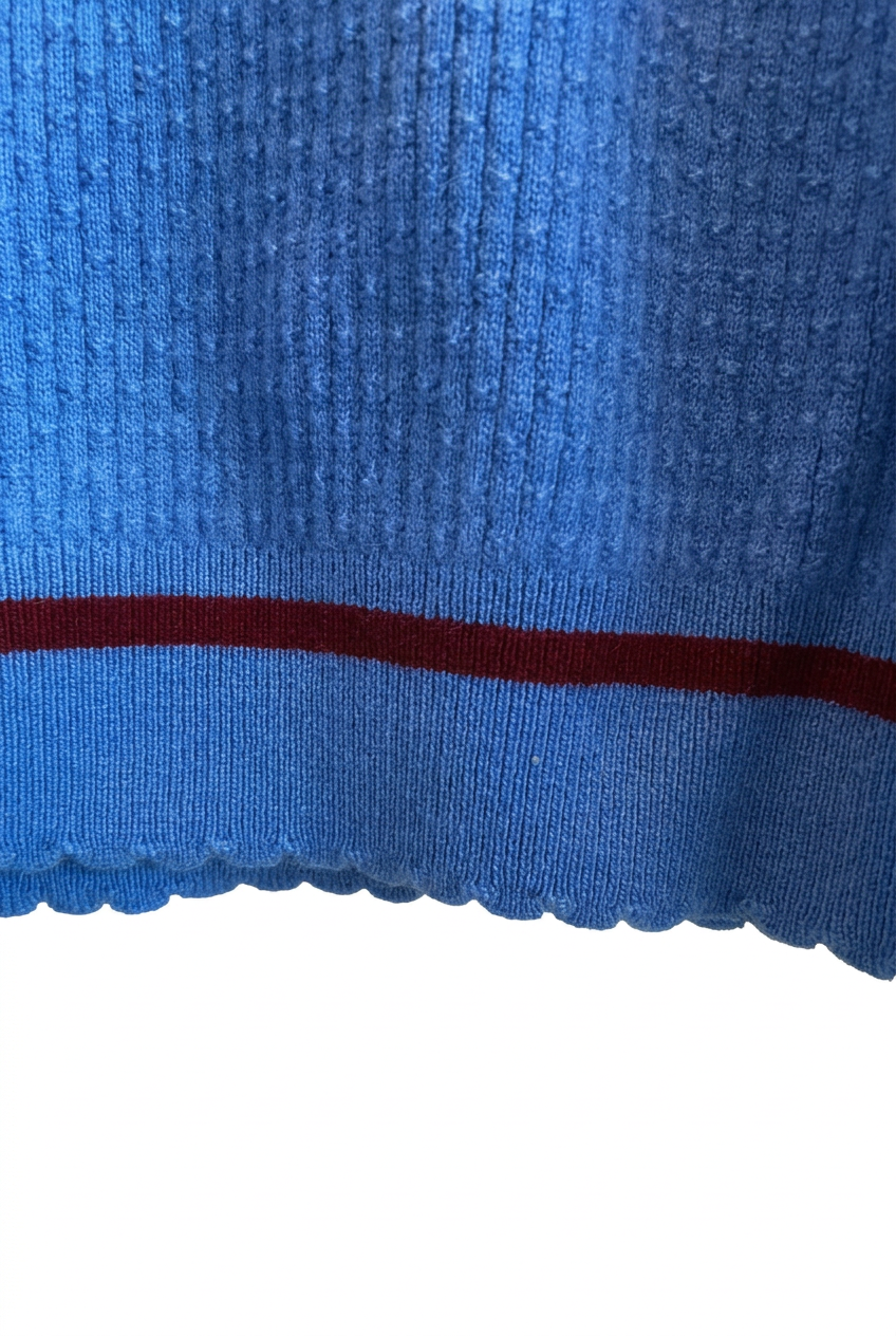 Close-up of the blue merino knit, burgundy stripe and scalloped hem on a white background.